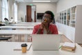 Thoughtful african american nerd man student studying in library using laptop. Royalty Free Stock Photo