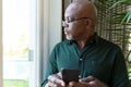 Thoughtful african american senior man holding smartphone ale looking outside window Royalty Free Stock Photo