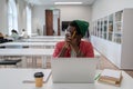 Thoughtful african american nerd man student studying in library using laptop. Royalty Free Stock Photo