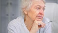Thoughtful aged lady with sad eyes wrinkly face alooks aside holding glasses in hand