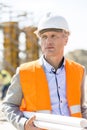 Thoughtful architect looking away while holding blueprints at construction site Royalty Free Stock Photo