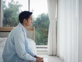 Thoughtful Asian man in denim shirt sitting on the bed feeling lonely.