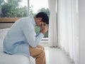 Thoughtful Asian man in denim shirt sitting on the bed feeling lonely.