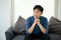 Thoughtful Asian man sits on a sofa, pondering and looking out the window Royalty Free Stock Photo