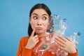 Thoughtful asian woman, holding plastic bottles, looking aside and thinking about recycling, sorting garbage, blue