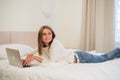 Thoughtful attractive blond woman using a laptop computer as she sits on the edge of a bed at home or in a hotel bedroom Royalty Free Stock Photo