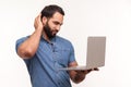 Thoughtful bearded man looking at laptop display rubbing his back of head, dont understand operation system, cant install