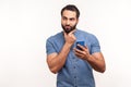 Thoughtful bearded man scratching chin holding smartphone in hand, contemplating about software updating, choosing suitable