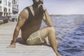 Thoughtful bearded man sitting on wooden pier on seaside and looking into the distance on the horizon in the sea. human