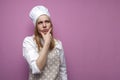 Thoughtful beautiful girl cook in kitchen clothes thinks over an idea on a pink background, a woman housewife dreams and looks at