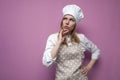 Thoughtful beautiful girl cook in kitchen clothes thinks over an idea on a pink background, a woman housewife dreams and looks at Royalty Free Stock Photo