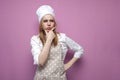 Thoughtful beautiful girl cook in kitchen clothes thinks over an idea on a pink background, a woman housewife dreams and looks at