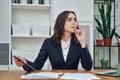 thoughtful beautiful young adult businesswoman manager in a suit with a tablet pc in office