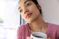 Thoughtful biracial woman holding cup of coffee and looking out window at sunny home Royalty Free Stock Photo