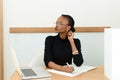 Thoughtful black businesswoman in glasses touching her neck looking away at desk with notepad and laptop in office Royalty Free Stock Photo