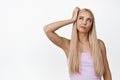 Thoughtful blond woman looking aside and scratching head, thinking, making decision, standing in pink tank top over Royalty Free Stock Photo