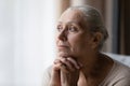 Thoughtful bored older 70s woman looking at window