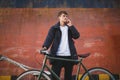 Thoughtful boy with brown hair standing with bicycle and dreamily looking aside talking on his cellphone. Young man in