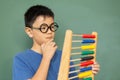 Thoughtful boy learning math with abacus against green chalkboard in a classroom Royalty Free Stock Photo
