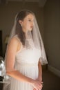 Thoughtful bride in wedding dress standing at home