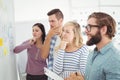 Thoughtful business people pointing at wall with sticky notes and drawings Royalty Free Stock Photo