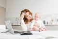 Thoughtful business woman holding her little baby while sitting at the table and working Royalty Free Stock Photo