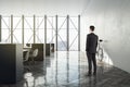 Thoughtful businessman standing in modern hipster coworking office interior with panoramic window and city view, wooden flooring, Royalty Free Stock Photo