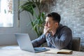 Thoughtful businessman touching chin, pondering ideas or strategy, sitting at wooden work desk with laptop, freelancer working on Royalty Free Stock Photo