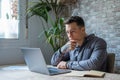 Thoughtful businessman touching chin, pondering ideas or strategy, sitting at wooden work desk with laptop, freelancer working on Royalty Free Stock Photo