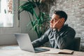 Thoughtful businessman touching chin, pondering ideas or strategy, sitting at wooden work desk with laptop, freelancer working on Royalty Free Stock Photo