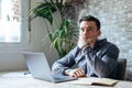 Thoughtful businessman touching chin, pondering ideas or strategy, sitting at wooden work desk with laptop, freelancer working on Royalty Free Stock Photo