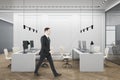 Thoughtful businessman walking in luxury coworking office interior with furniture, wooden flooring, concrete walls, equipment and Royalty Free Stock Photo