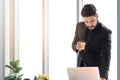 Thoughtful businessman wearing black suit and holding paper coffee cup, checking documents in laptop computer stand at office desk Royalty Free Stock Photo