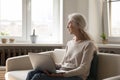 Thoughtful calm older 70s laptop user woman sitting on sofa