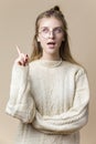 Thoughtful Caucasian Blond Female Wearing Knitted Decorated Warm Sweater And Glasses while Looking Aside with Lifted Finger Over Royalty Free Stock Photo