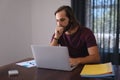 Thoughtful caucasian man sitting at table working from home and using laptop Royalty Free Stock Photo