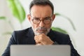 A thoughtful mature man in a smart casual suit with glasses, deeply concentrating on his laptop Royalty Free Stock Photo