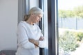 Thoughtful caucasian senior woman with arms crossed looking out of the window at home Royalty Free Stock Photo