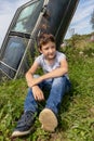 Thoughtful caucasian teenage boy sitting on the grass in countyside in summer day with serious face expression, a retro car is on Royalty Free Stock Photo