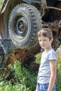 Thoughtful caucasian teenage standing on the grass in countyside in summer day with serious face expression, a retro car is on