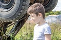 Thoughtful caucasian teenage standing on the grass in countyside in summer day with serious face expression, a retro car is on