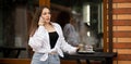 Thoughtful caucasian woman calling on mobile phone while looking near the coffee shop window during coffee break. Street Royalty Free Stock Photo