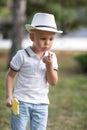 Thoughtful child blowing at his finger. Boy with a lollipop on a green park background. A cute boy outdoors in summer.