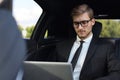 Thoughtful confident businessman sitting in the luxe car and using his laptop Royalty Free Stock Photo