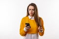 Thoughtful confused young brunette woman holding her smart phone. Technology, youth and communication concept Royalty Free Stock Photo