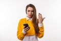 Thoughtful confused young brunette woman holding her smart phone. Technology, youth and communication concept Royalty Free Stock Photo