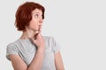 Thoughtful contemplative woman stands sideways, keeps index finger on lips, dressed in grey t shirt, contemplates about something Royalty Free Stock Photo