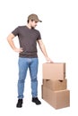 Thoughtful delivery man wearing cap, full length portrait, stands near cardboard parcel boxes, isolated on white background. Royalty Free Stock Photo