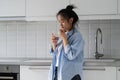 Thoughtful emotionless Asian woman taking medicine and drinking water standing in kitchen near sink