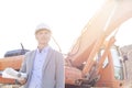 Thoughtful engineer looking away while holding blueprints by bulldozer at construction site Royalty Free Stock Photo